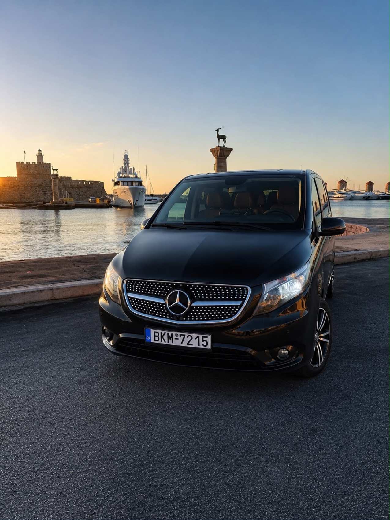 Black Mercedes van parked at Mandraki harbour in Rhodes at sunset, with the fortress and deer column behind