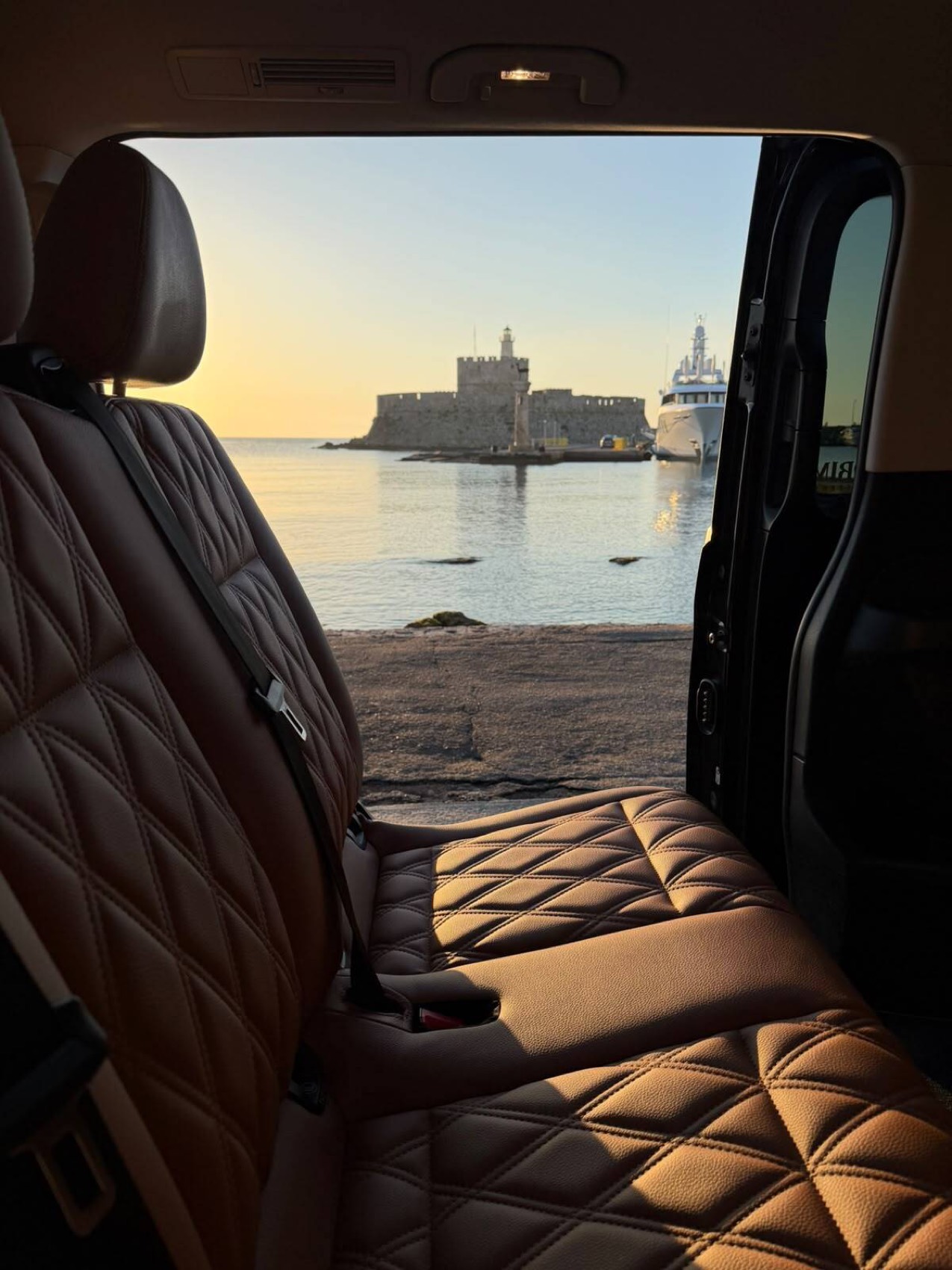 Quilted tan leather seats inside the van, sliding door open to a view of the sea and the fort of Saint Nicholas