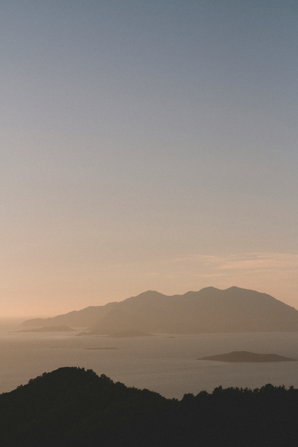 Mountain ridges fading into haze over the sea, seen from a hilltop