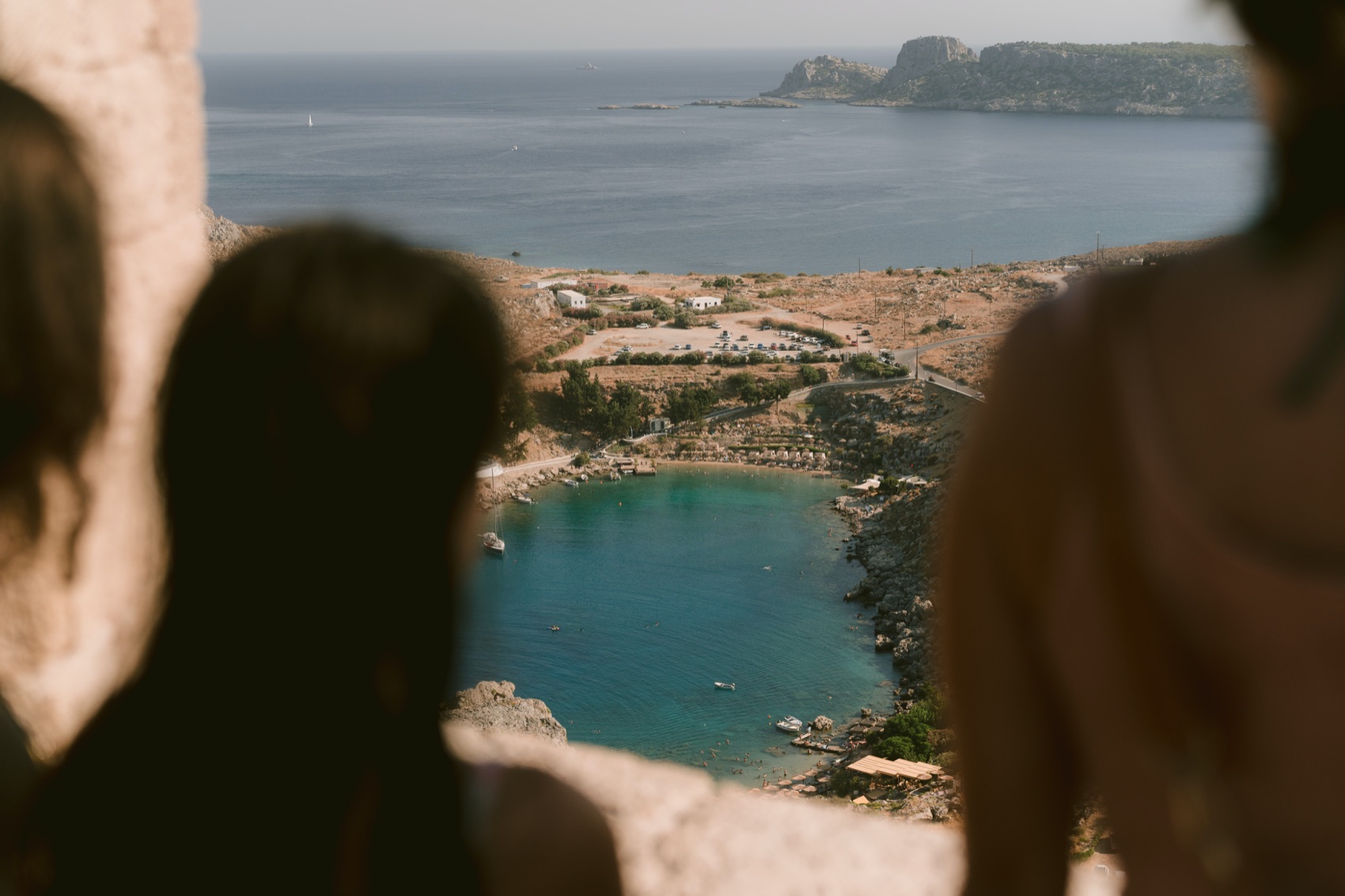 Two people looking down over the bay of Lindos from a viewpoint