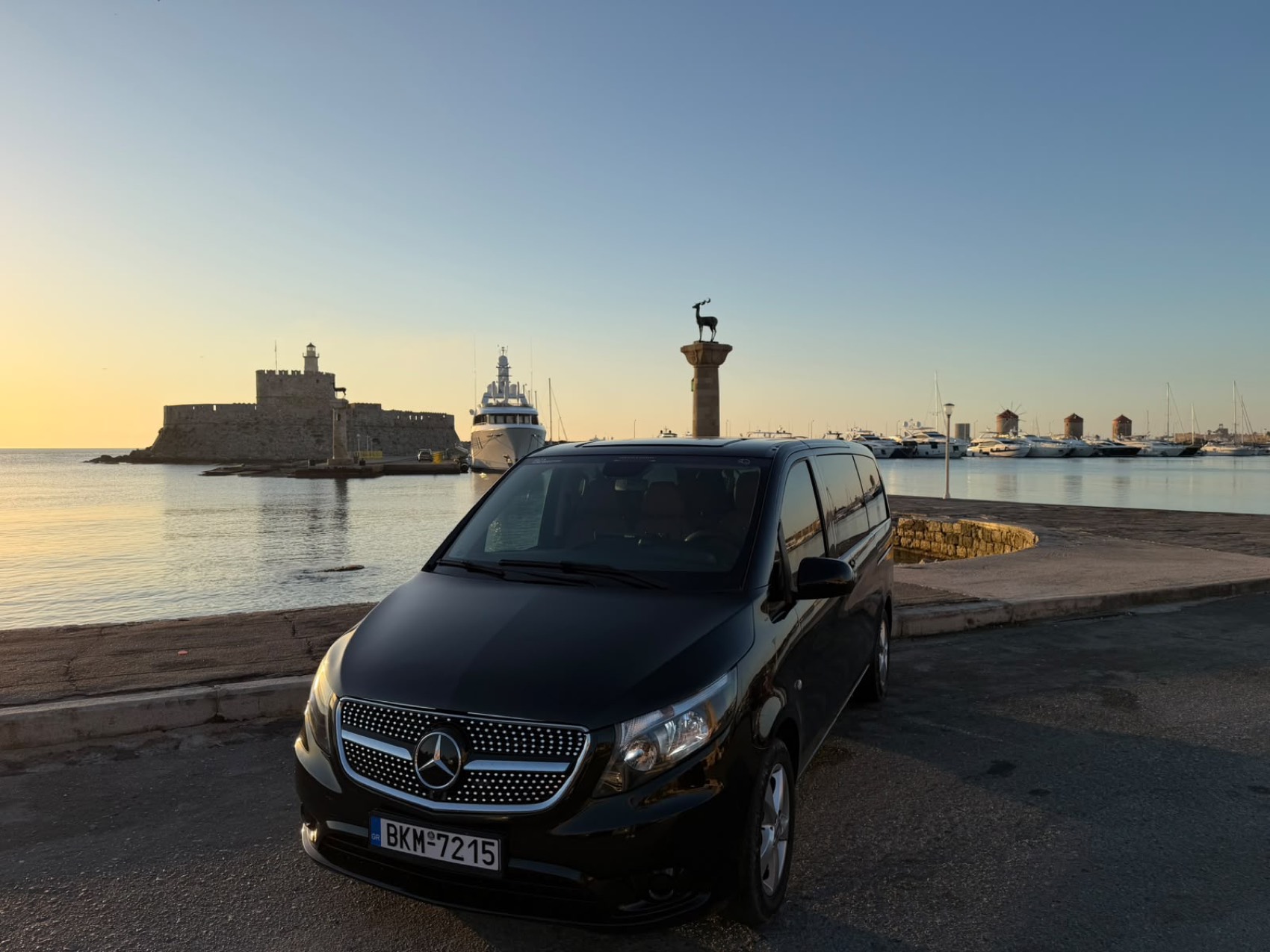 Mercedes van on the quay at Mandraki harbour with yachts and the old windmills in the background